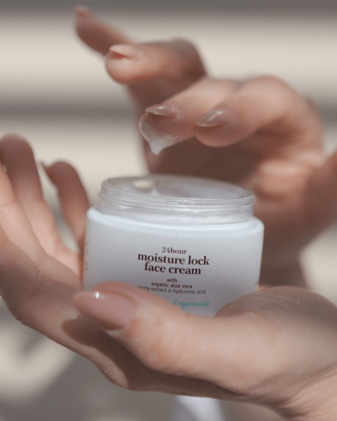 Hand holding a jar of 24-hour moisture lock face cream with a blurred background