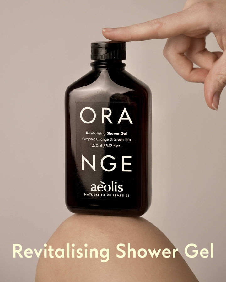 Bottle of Aeolis Orange Revitalizing Shower Gel held by a hand on a beige background