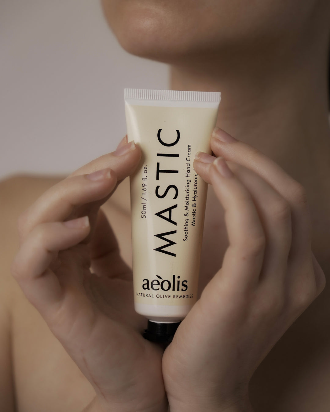 Hand holding a tube of Mastic hand cream by Aeolis against a neutral background