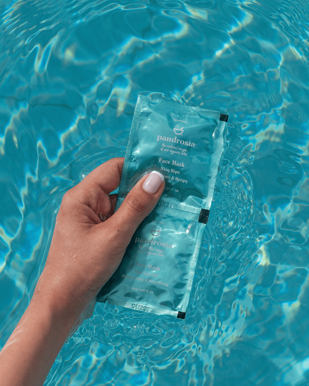 Hand holding a blue skincare packet with water in the background