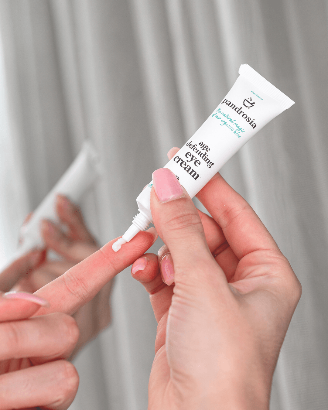 Hand holding a tube of eye cream with a neutral background