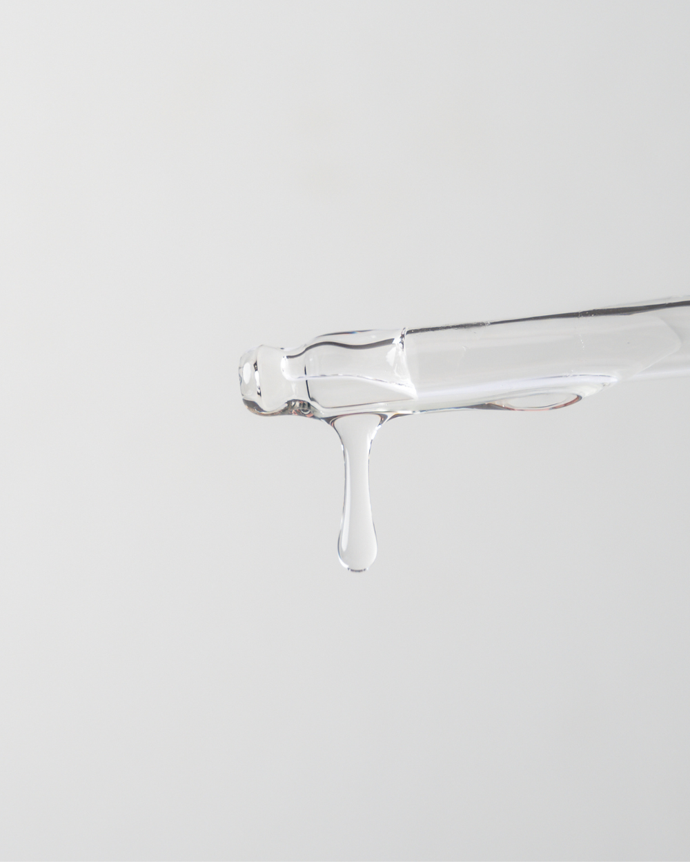 Clear glass container with a small amount of liquid on a light gray background