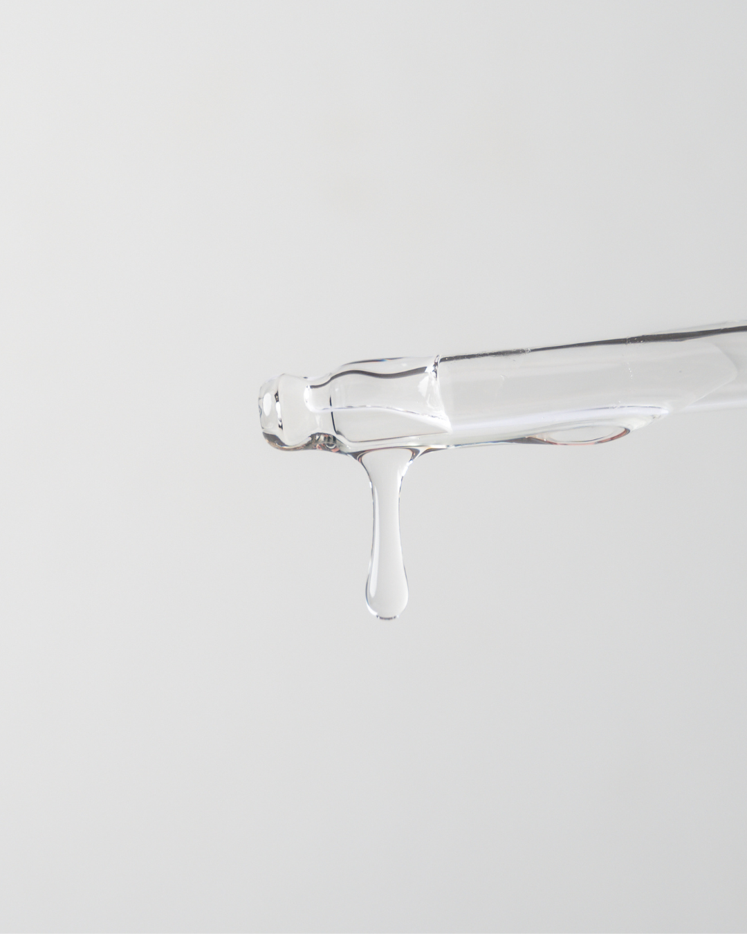 Clear glass container with a small amount of liquid on a light gray background
