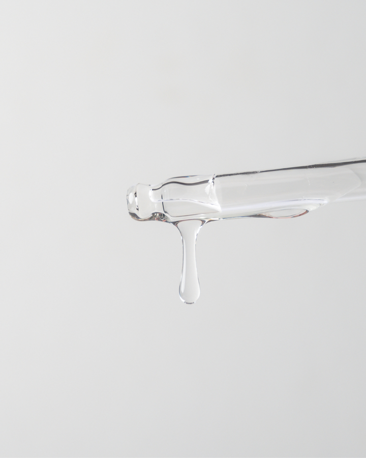Clear glass container with a small amount of liquid on a light gray background