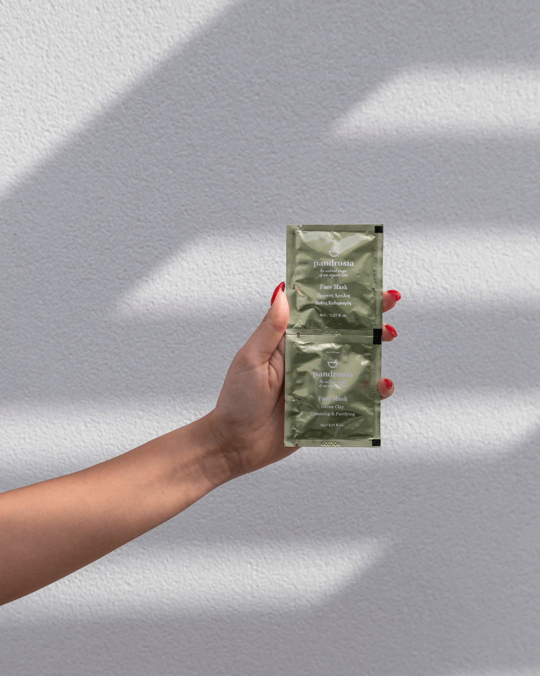 Hand holding two green skincare packets against a light gray background