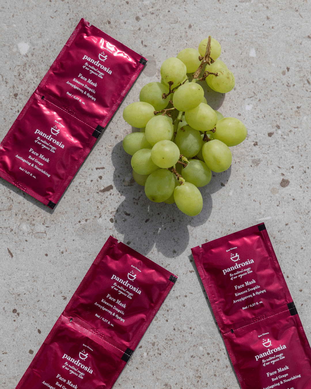 Three red face mask packets and a bunch of green grapes on a concrete surface